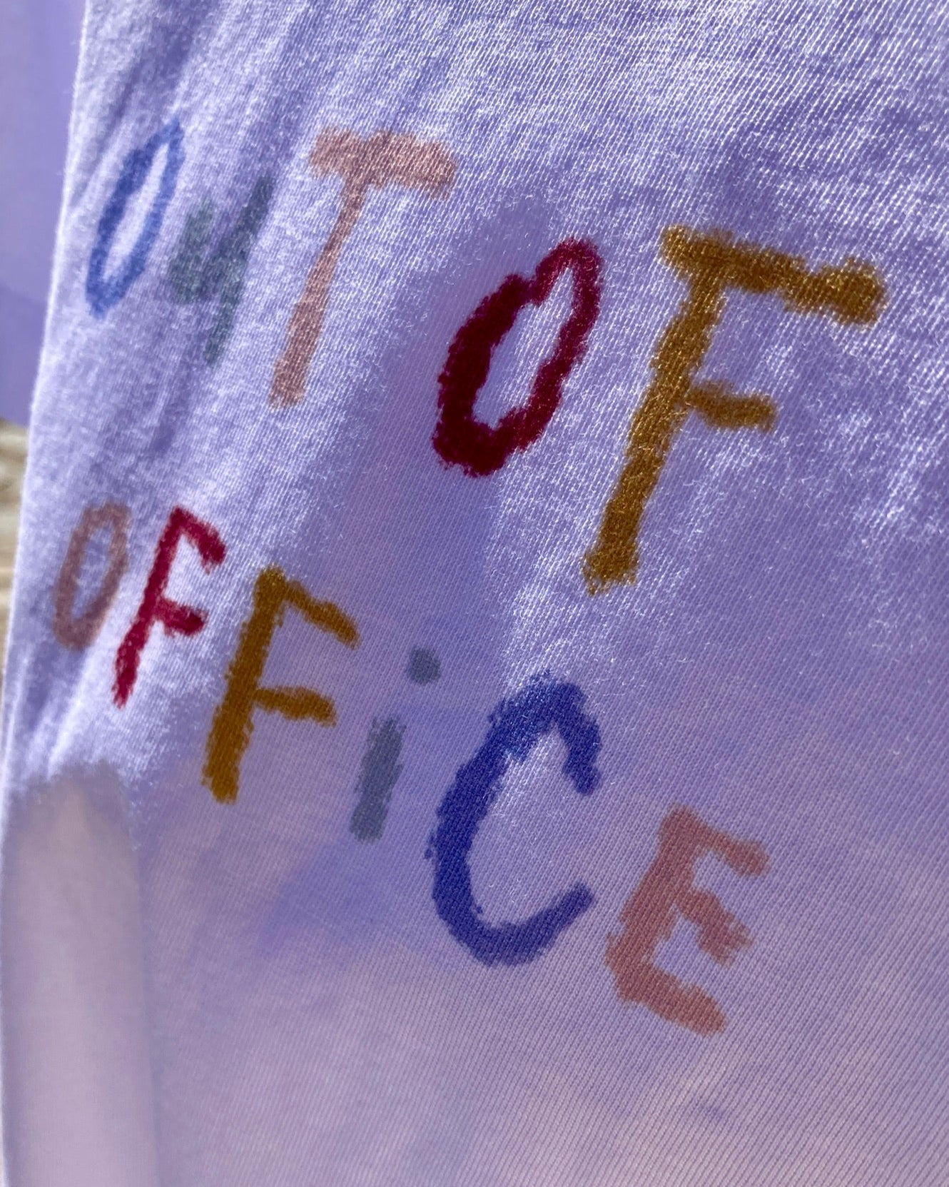Text 'OUT OF OFFICE' on a T-shirt with multicolor letters.